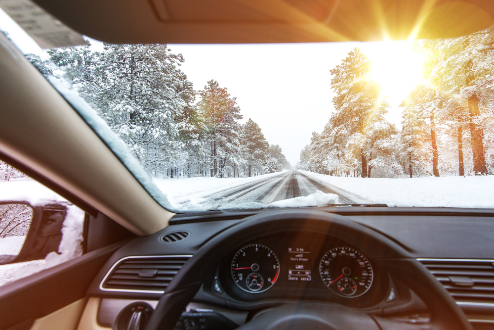 The inside of a car facing outward a the break of a snowy dawn. Winter hangs in the air behind the steering wheel.