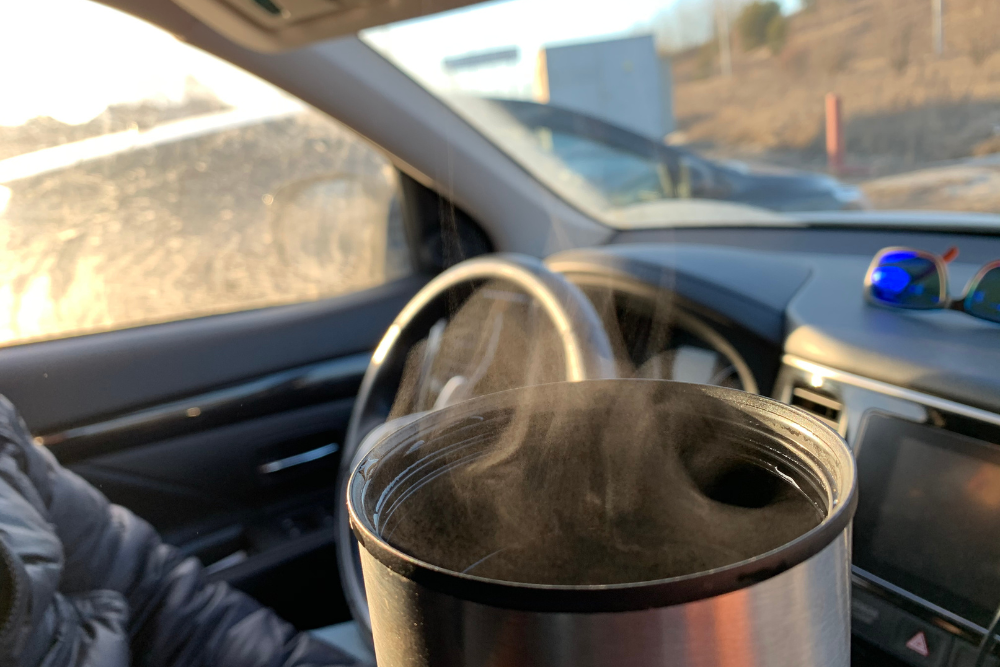 From the passenger's seat of a car, steam rises from the mouth of a travel mug on a chill morning.