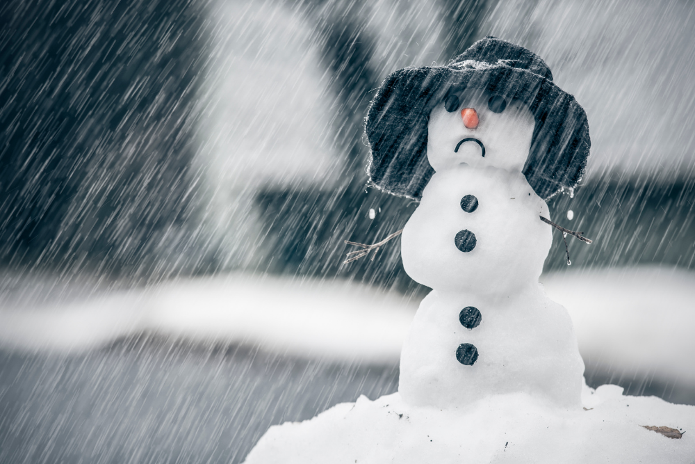 A snowman wears a rainhat and a frown as he gets rained on.